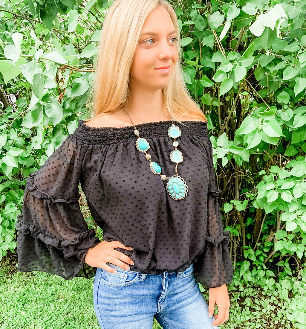 Side view of a young woman wearing a black shoulder bell sleeve top.