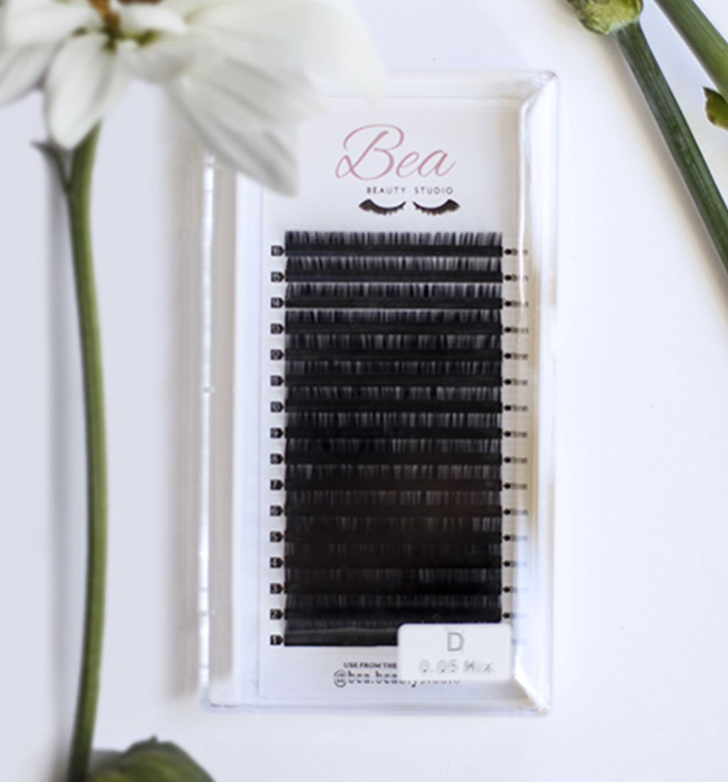 D Curl Lash Tray .18 on a white background  surrounded by flowers.